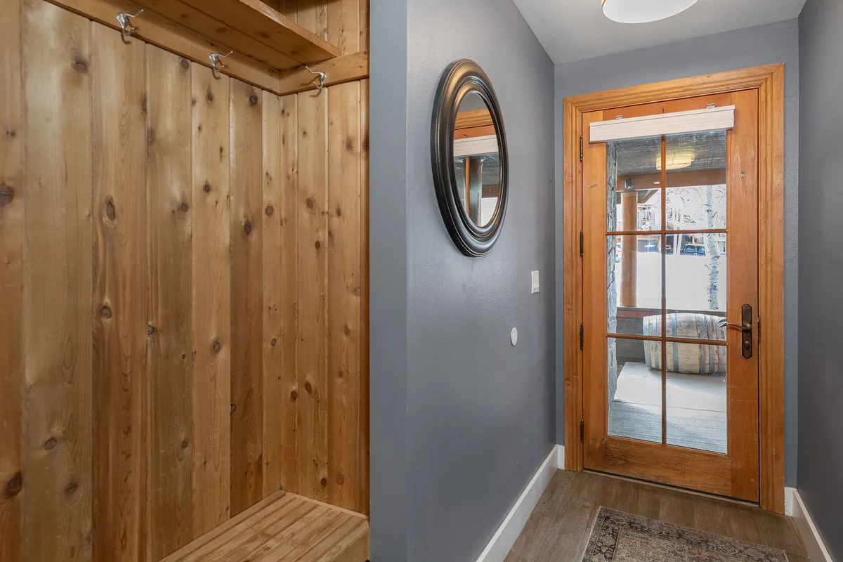 A warm and inviting entryway with wood paneling, a round mirror, and a front door featuring glass panels. The hooks and open area make this space ideal for dropping off hiking packs, boots, or jackets after returning from the trails.