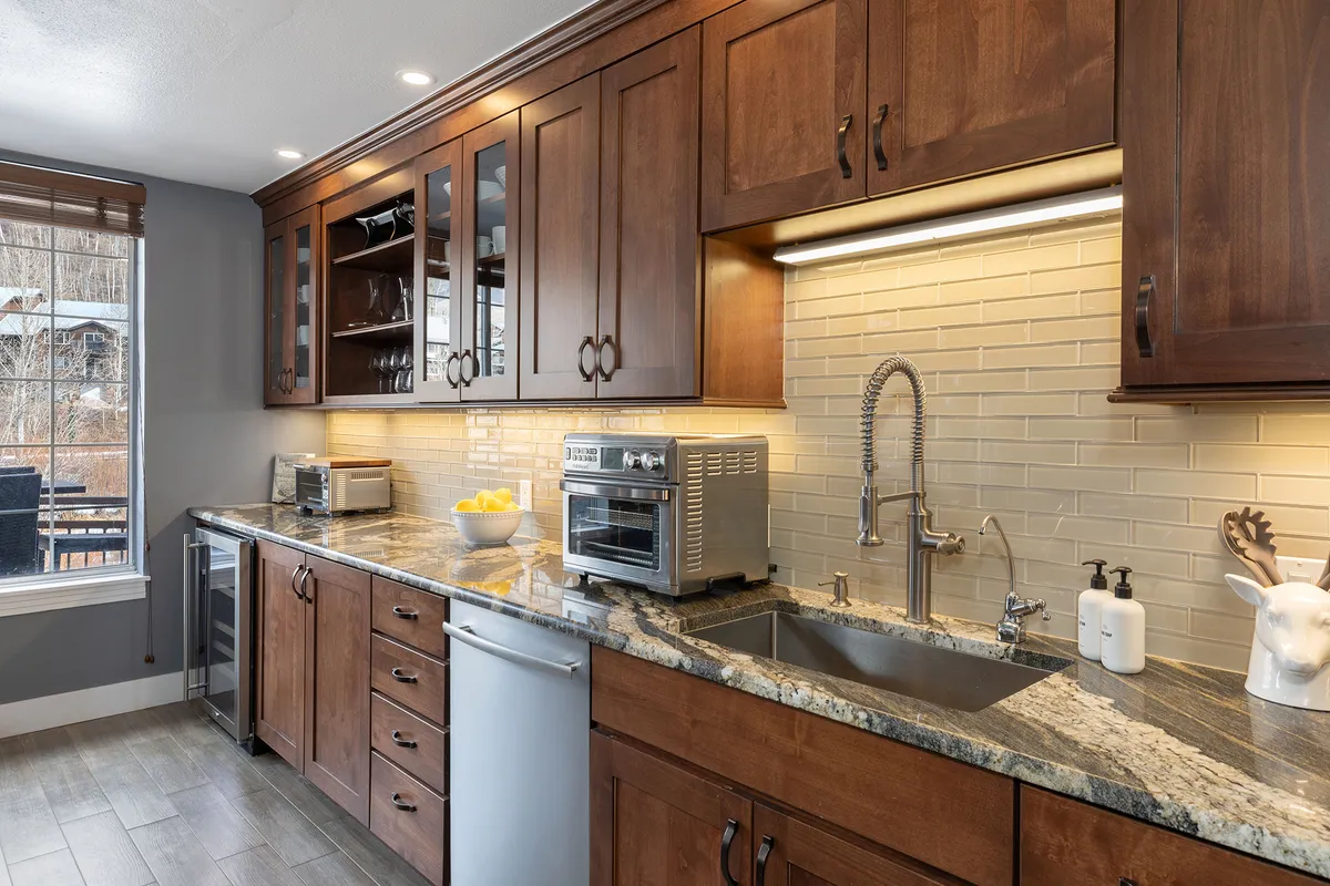 An open kitchen with granite countertops, stainless steel appliances, and wood cabinetry. A window lets in natural light and offers a view, while the setting suggests this is an active, social space ideal for cooking with loved ones or watching children play as meals are prepared.