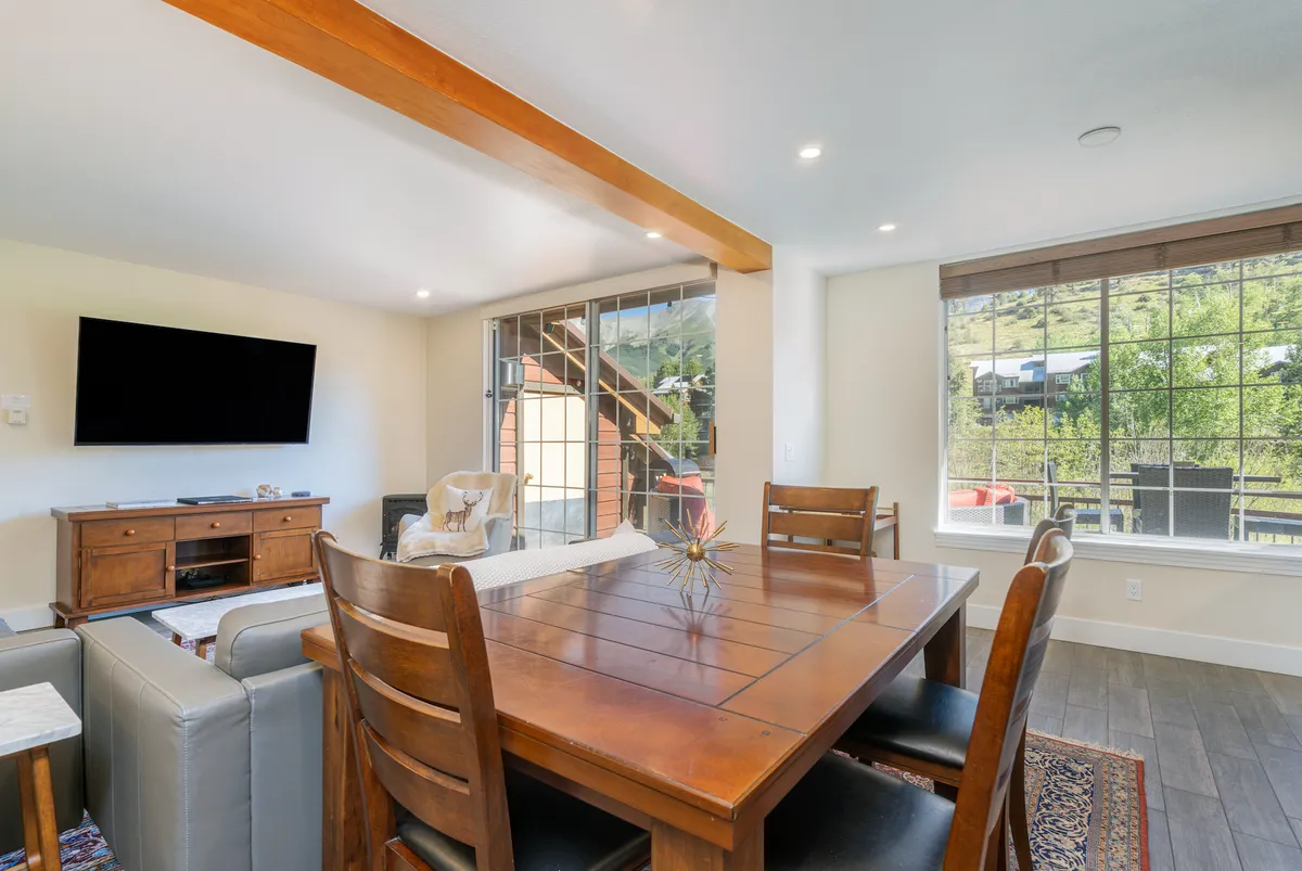 A bright dining area with a large table, TV on the wall, and an expansive window framing an outdoor view. The natural light and setting make it ideal for family breakfasts or evening gatherings with a view of the surrounding landscape.