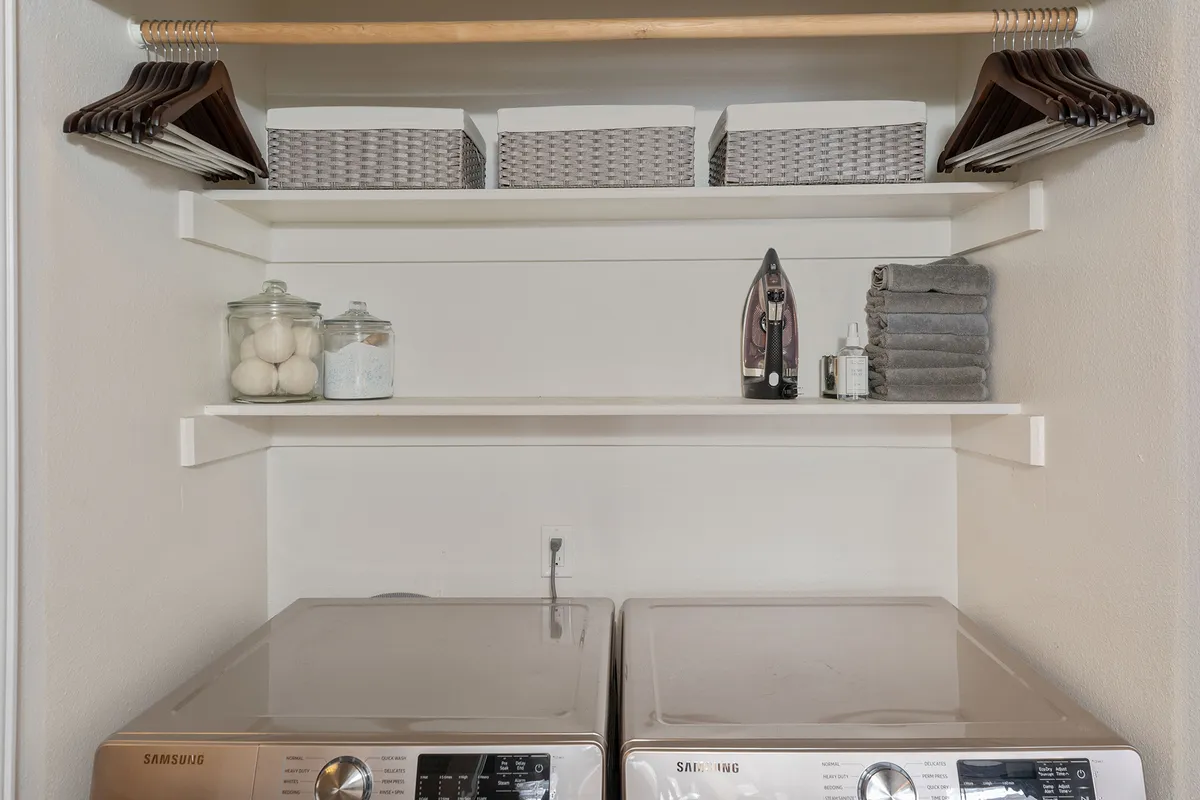 A tidy laundry room with washing machines, a shelf for storage boxes, and neatly arranged towels and an iron. The setup is clean and efficient, supporting easy post-adventure cleanup.