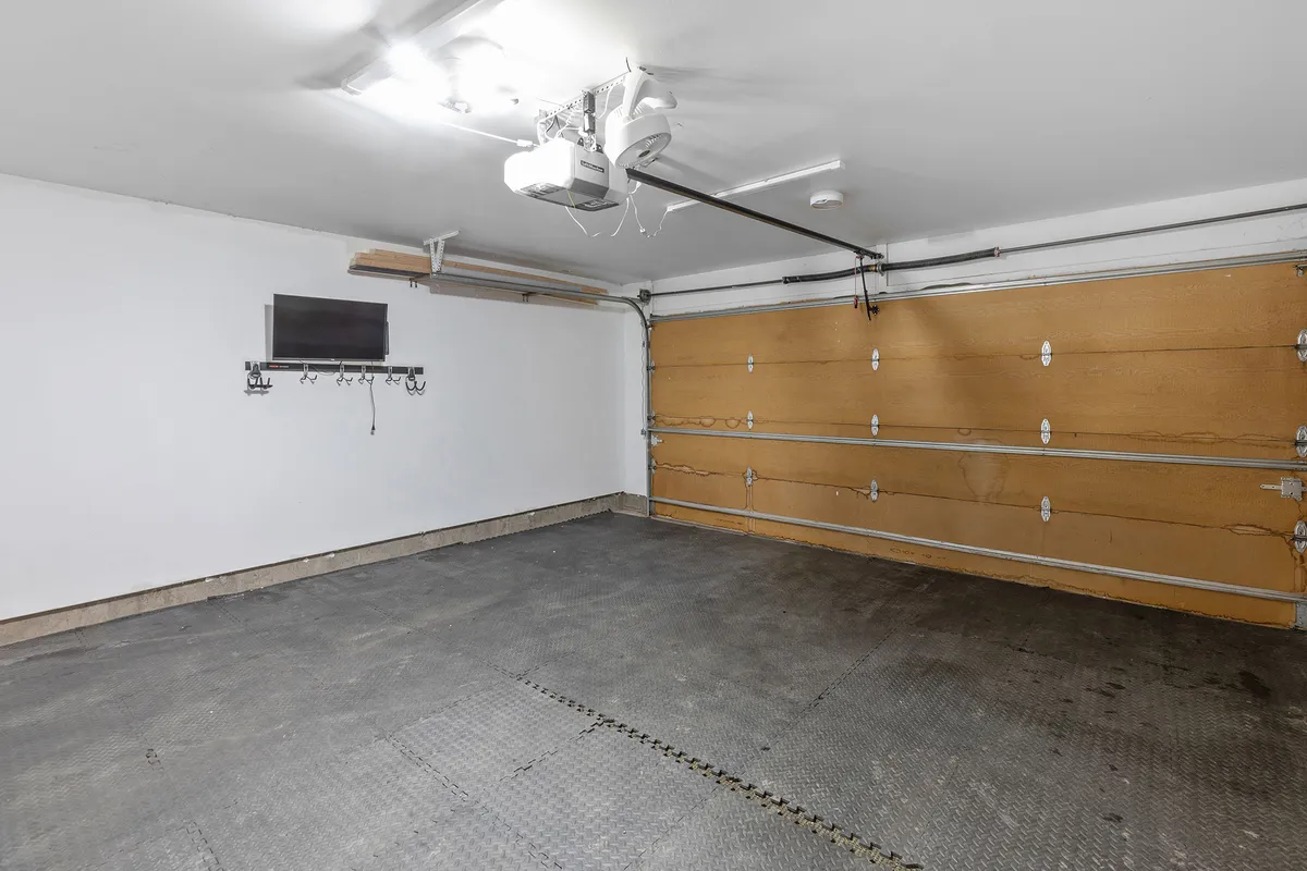 This image displays a garage space with visible wall hooks and a mounted TV, offering a practical, organized area for storing bikes, skis, snowboards, and other adventure gear. The space is clean, functional, and ready for easy access to equipment.