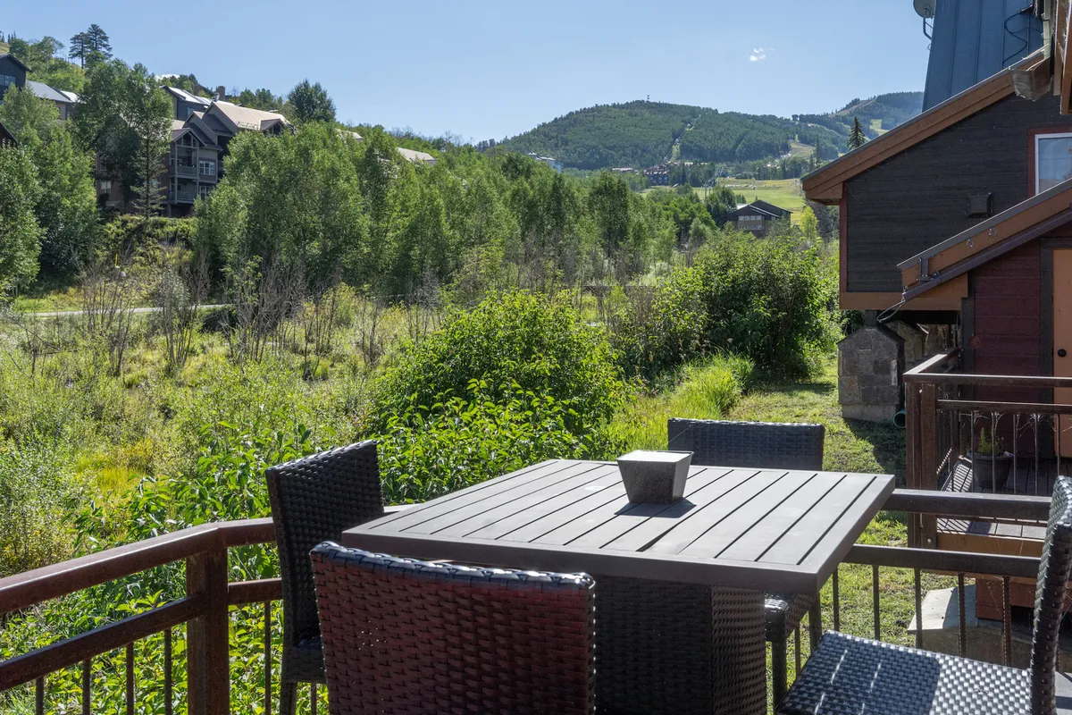 This exterior image showcases an outdoor dining table surrounded by lush greenery with a spectacular mountain view in the background. The setting feels open, inviting, and family-friendly, ideal for shared meals or children playing in the fresh air.