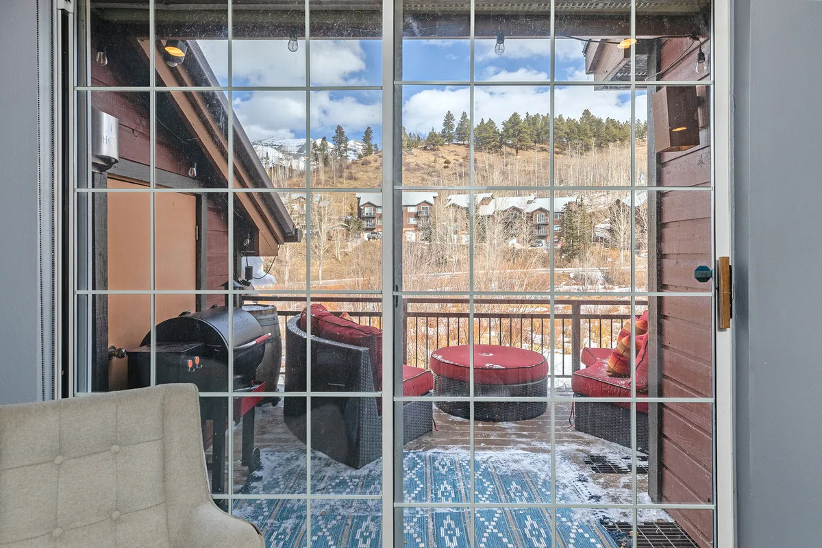 Glass doors open onto a private balcony featuring outdoor seating, a grill, and a decorative rug. The balcony is situated to take in sweeping views, inviting guests to savor sunsets or enjoy al fresco dining.